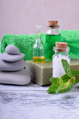 Fototapeta na wymiar Spa set: massage stones, aromatic oil, sea salt, green gel, organic soap and green towel on white wooden table