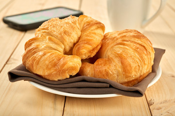 Coffee cup and fresh baked croissants on wooden table