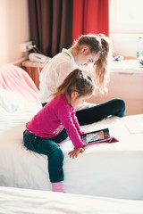Teenage girl using mobile phone together with her little sister watching animated movie on tablet