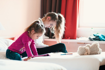 Teenage girl using mobile phone together with her little sister watching animated movie on tablet