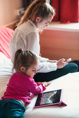 Teenage girl using mobile phone together with her little sister watching animated movie on tablet