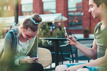 Teenage girl and boy,  having fun using smartphones sitting in center of town