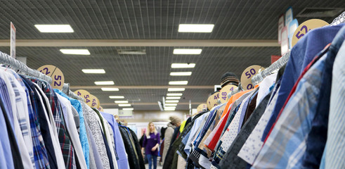 Elegant shirts hanging in two rows on hangers in the store are blurry. In the background are blurred buyers. On the eve of Black Friday. Background for design from a department store.