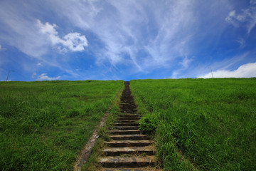 Fototapeta na wymiar line of stair from ground up to to of mountain , outdoor background show brown stair in the middle of green field in sunny day