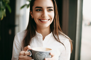 Close up portrait of a amazing female freelancer looking away smiling while holding a cup of coffee while working in a coffee shop.