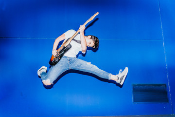 young man jumping with electric guitar on blue background