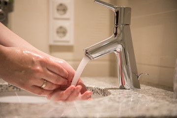 Frau nutzt Waschbecken mit Wasserhahn und Leitungswasser zum Händewaschen