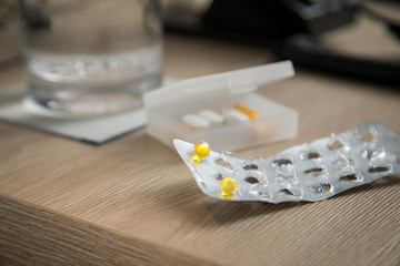 Fototapeta na wymiar Pillen Blister mit gelben Tabletten und Wasser Glas auf Holz Nachttisch