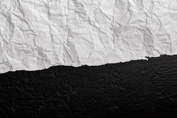 White crumpled paper against a wall in black. View from above