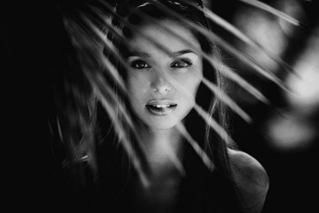 Black and white fashion portrait of beautiful young blonde girl standing in palms and watching with...