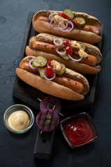Black wooden serving tray with hot-dogs, studio shot on a black stone background