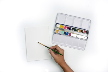 Top view watercolor painting, a hand holding a brush for painting art on the white paper, using a colorful watercolor palette set, on white background. Art and craft concept.