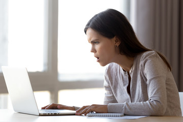 Annoyed female sitting at desk looking on laptop screen