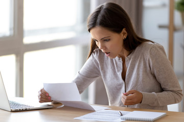 Surprised young woman sitting at desk reading letter