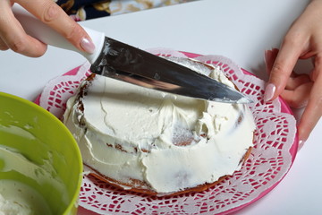 Baked biscuit cake. A woman smears it with white cream.