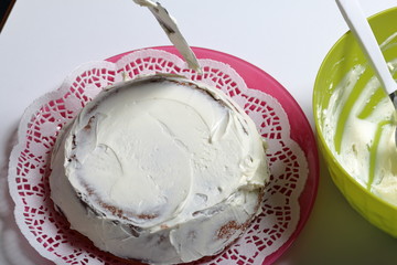 Baked biscuit cake. A woman smears it with white cream.