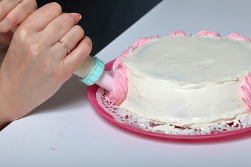 A woman is holding a pastry bag with cream. Decorates with his cake.