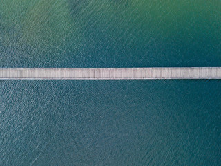 Aerial view of pedestrian bridge over lake. Narrow wooden bridge with beautiful seafloor and reflection