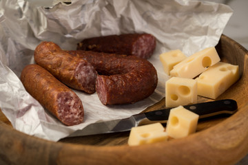 Ringwurst Salami, Bierbeißer Wurst und Edamer Käse in Wachspapier mit Messer auf Vesper Holzbrett