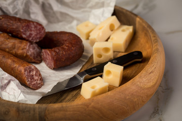 Ringwurst Salami, Bierbeißer Wurst und Edamer Käse in Wachspapier mit Messer auf Vesper Holzbrett