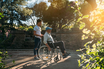 56 year old male sitting on a wheelchair and he young friend in the park