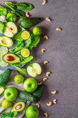 Slice and whole avocado, green apples, lime, spinach and cashew nuts on a gray background with free space for the text. top view