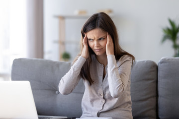 Annoyed young woman sitting on couch touch temples feels unwell