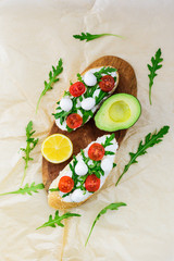 Sandwiches with tomato, mozzarella, arugula and curd cheese on a wooden board