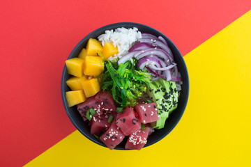 Poke bowl with tuna in the dark bowl in the center of the colorful background.Top view.Closeup.