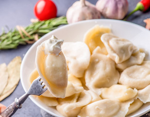 boiled dumplings with filling and sauce on a fork on the background of a full plate