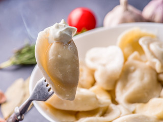 boiled dumplings with filling and sauce on a fork on the background of a full plate