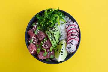 Poke bowl with tuna in the white bowl in the center of the yellow background.Top view.Closeup.