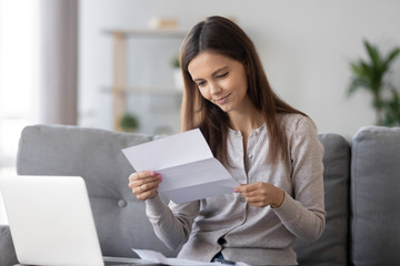 Young attractive woman sitting on couch smiling reading letter