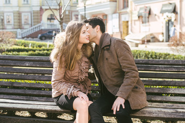 Young multiracial couple, male and female heterosexual students in love. A date in a city park on a wooden bench. Young brunette man with dark skin and a Caucasian woman in an embrace on a sunny day