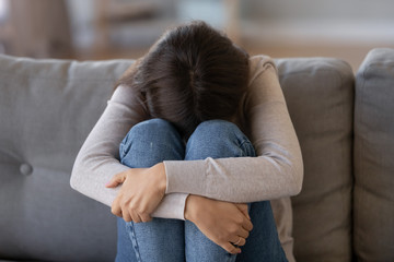 Depressed woman sitting on couch feeling unhappy crying alone