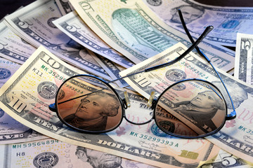 Sunglasses is placed on the banknote of US dollars spread around