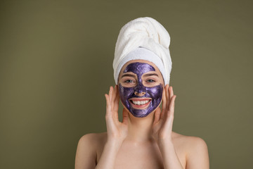 Face care and beauty treatments. Happy woman with purple cloth moisturizing mask on her face