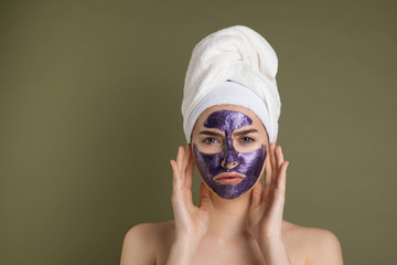 Attractive unhappy young woman with purple face mask and shower towel on her head