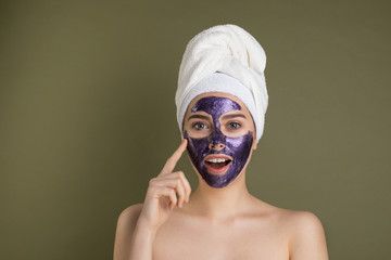 Portrait of a happy and positive naked girl with a purple clay cosmetic mask on her face