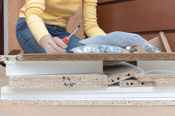 Woman sitting on the floor at home and assembling furniture using hand tools