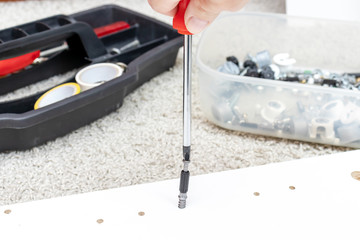 Assembling white furniture, she tighten a screw with a screwdriver, close up view