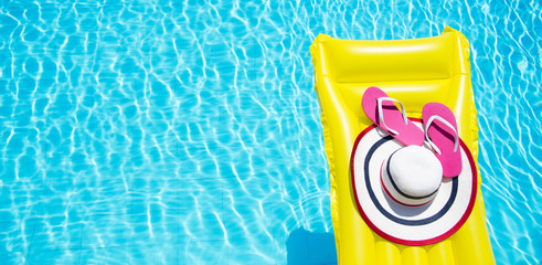 Beach summer holiday background. Inflatable air mattress, flip flops and hat on swimming pool. Yellow lilo and summertime accessories on poolside. Top view and copy space. Banner