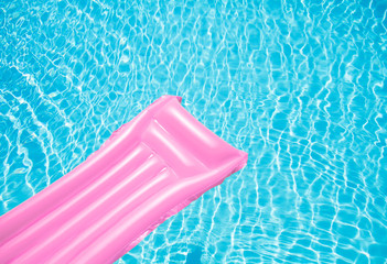 Beach summer holiday background. Inflatable air mattress on swimming pool water. Pink lilo and summertime accessories on poolside. Top view and copy space