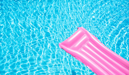 Beach summer holiday background. Inflatable air mattress on swimming pool water. Pink lilo and summertime accessories on poolside. Top view and copy space. Banner