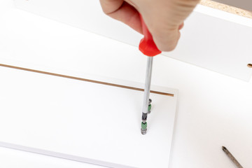 Assembling white furniture, she tighten a screw with a screwdriver, close up view