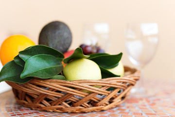 A glass and a wicker basket with fruit on a street table with a mosaic.