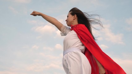 Fototapeta na wymiar girl dreams of becoming a superhero. beautiful superhero girl standing on a field in a red cloak, cloak fluttering in the wind. Slow motion. young woman plays in red cloak with expression of dreams.