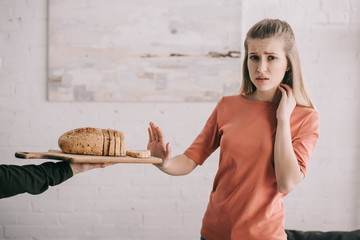 cropped view of man holding cutting board with sliced bread near sad blonde woman with gluten allergy - obrazy, fototapety, plakaty