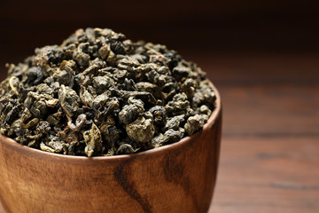Bowl of Tie Guan Yin oolong tea leaves on wooden background, closeup. Space for text