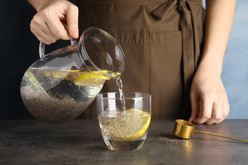 Young woman pouring water with chia seeds and lemon into glass at table, closeup